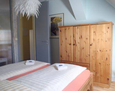 Doppelbett vor Holzschrank und Zimmertür